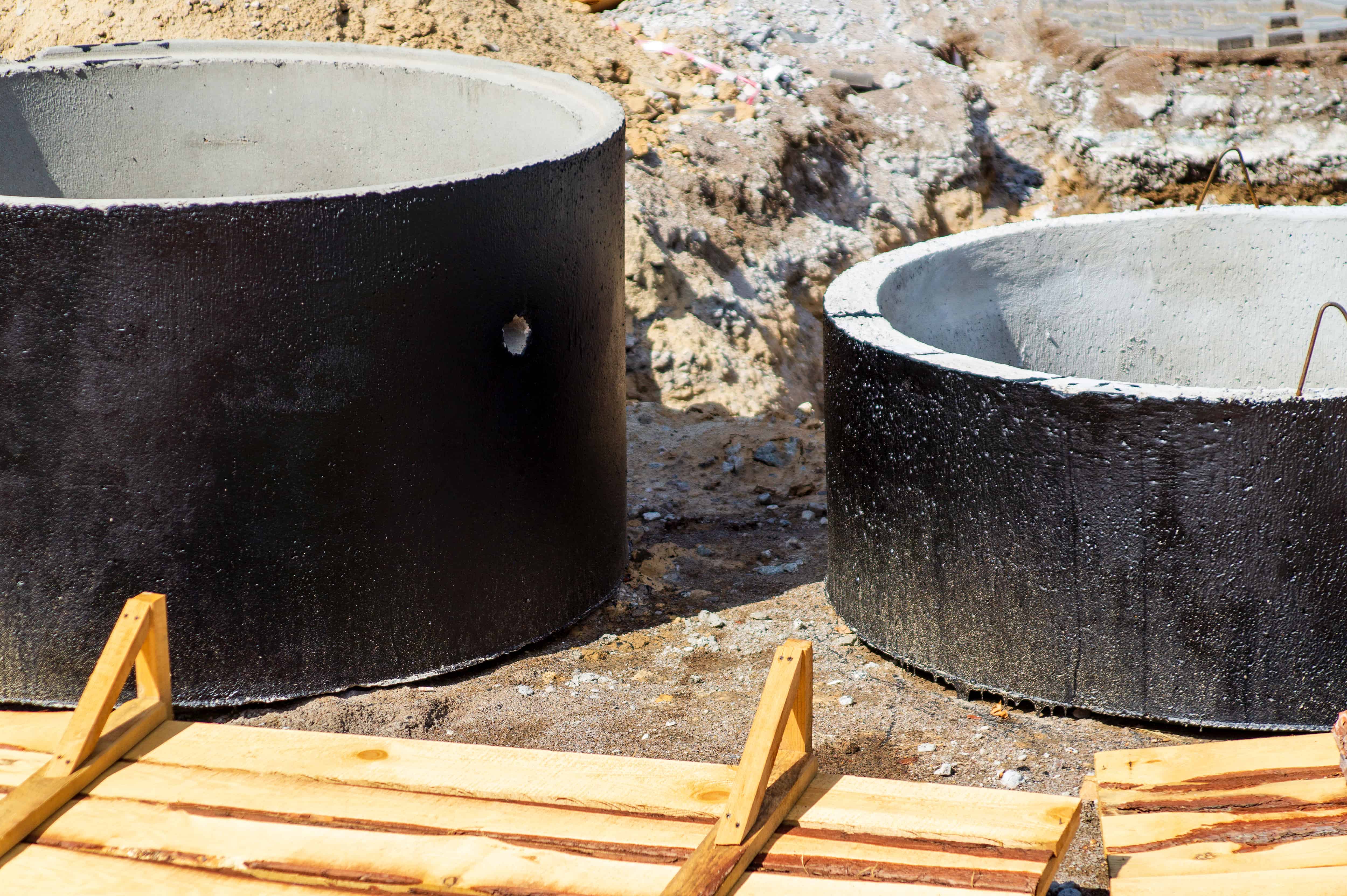 Two large, circular concrete pipes, partially coated with black sealant, are positioned vertically on a construction site. These structures often signify the installation process for cesspool services in Suffolk County.