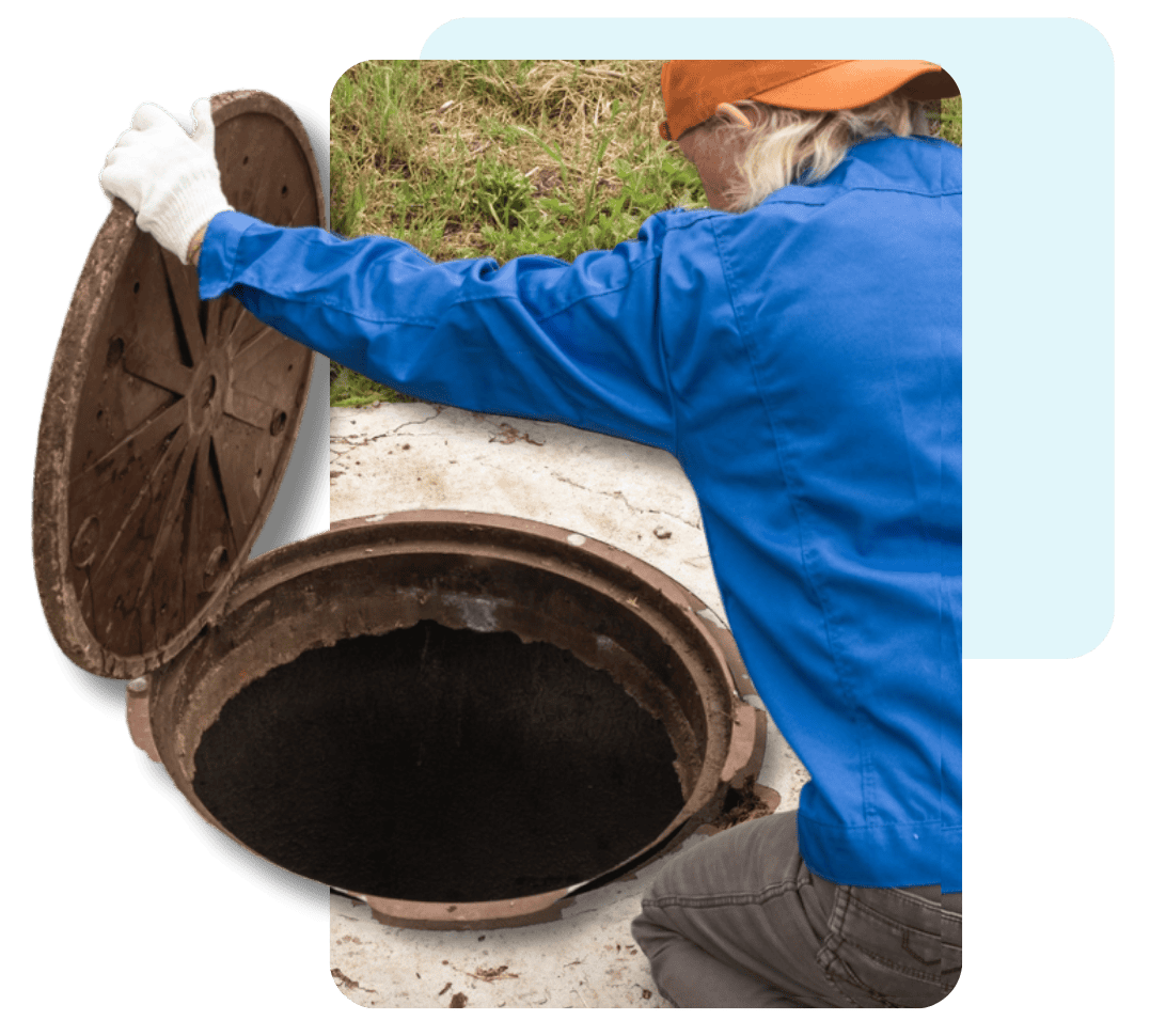 A person in a blue shirt and orange hat, wearing white gloves, is opening a circular outdoor manhole for septic tank pumping.
