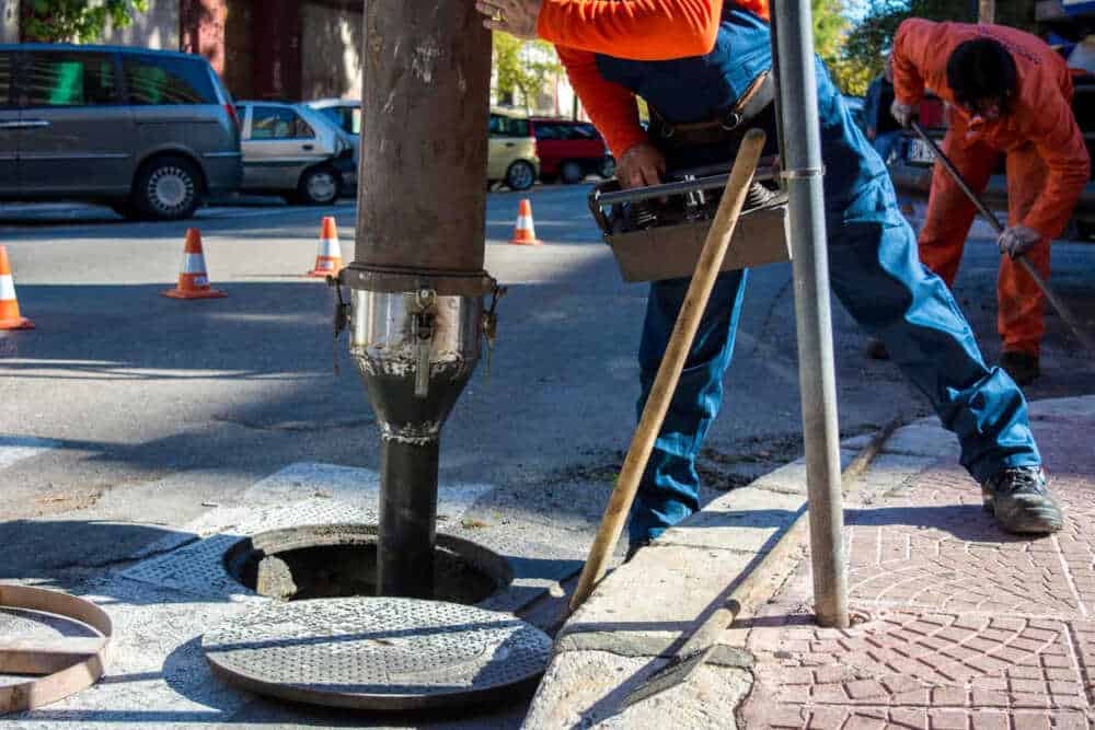 Two utility workers are servicing an underground system via a maintenance hole on a city street.