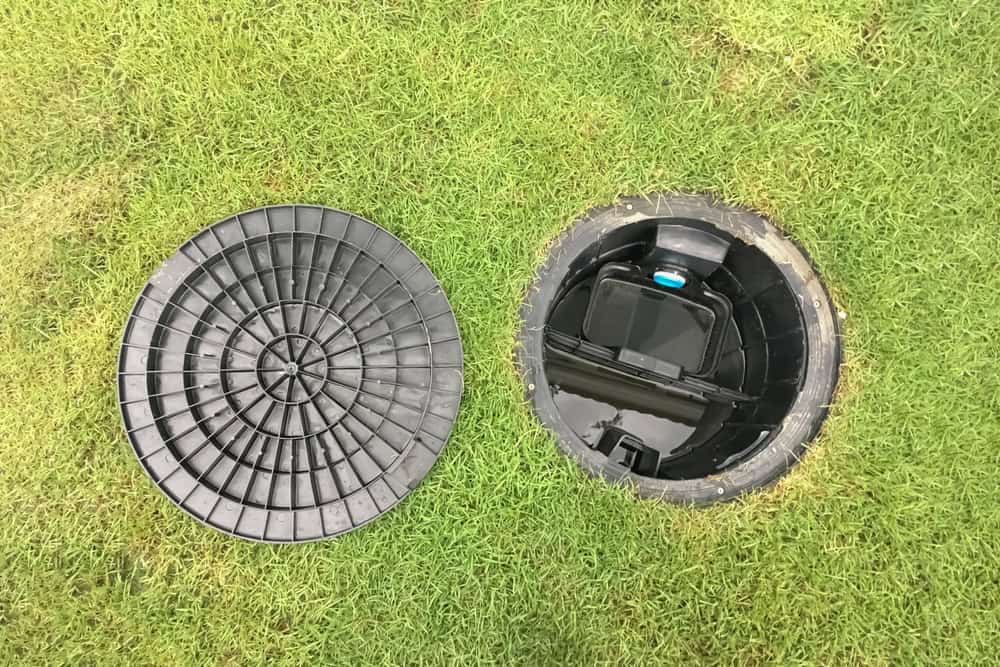 An open irrigation valve box in a grassy lawn, with the cover placed to the side.