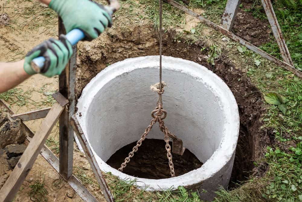 A worker with green gloves uses a tool near a septic tank under construction.